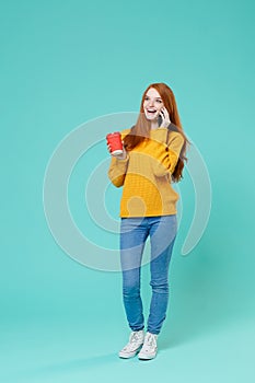 Cheerful young redhead girl in yellow sweater isolated on blue turquoise background studio portrait. People lifestyle