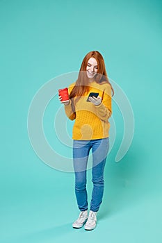 Cheerful young redhead girl in yellow sweater isolated on blue turquoise background studio portrait. People lifestyle