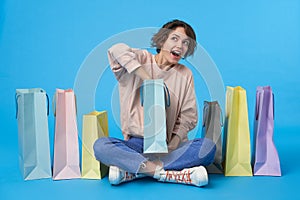 Cheerful young short haired curly female with casual hairstyle looking wonderingly what is inside of paper bag in her hands,