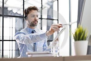 Cheerful young support phone male operator in headset, at workplace while using computer