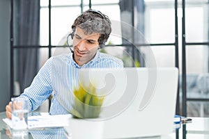 Cheerful young support phone male operator in headset, at workplace while using computer, help service and client
