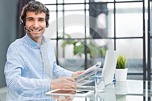 Cheerful young support phone male operator in headset, at workplace while using computer, help service and client