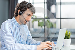 Cheerful young support phone male operator in headset, at workplace while using computer, help service and client