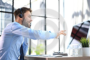 Cheerful young support phone male operator in headset, at workplace while using computer, help service and client