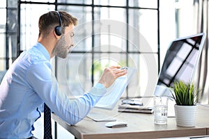 Cheerful young support phone male operator in headset, at workplace while using computer, help service and client