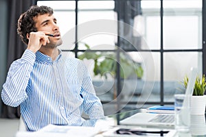 Cheerful young support phone male operator in headset, at workplace while using computer, help service and client