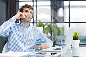 Cheerful young support phone male operator in headset, at workplace while using computer, help service and client