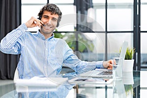 Cheerful young support phone male operator in headset, at workplace while using computer, help service and client