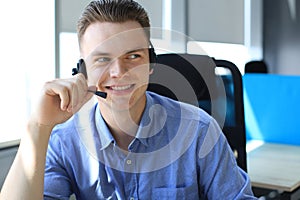 Cheerful young support phone male operator in headset, at workplace while using laptop