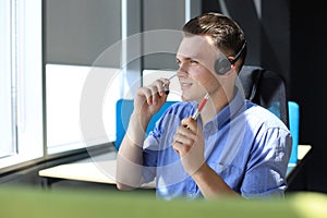 Cheerful young support phone male operator in headset, at workplace while using laptop