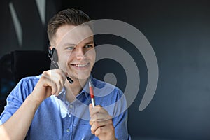 Cheerful young support phone male operator in headset, at workplace while using laptop