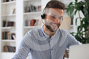 Cheerful young support phone male operator in headset, at workplace while using laptop