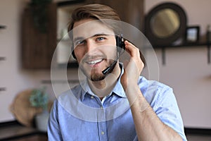 Cheerful young support phone male operator in headset, at workplace while using laptop