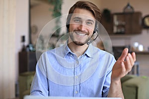 Cheerful young support phone male operator in headset, at workplace while using laptop