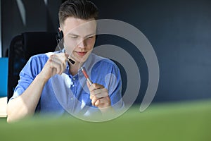 Cheerful young support phone male operator in headset, at workplace while using laptop, help service