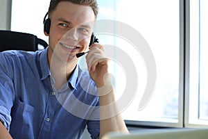 Cheerful young support phone male operator in headset, at workplace while using laptop, help service