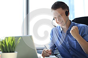 Cheerful young support phone male operator in headset, at workplace while using laptop, help service