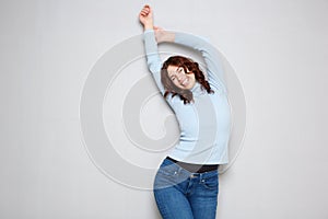 Cheerful young woman with arms raised against gray background