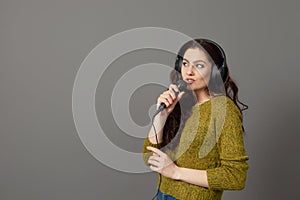 Cheerful young woman in casual clothes with headphones sing song in microphone, mock up copy space