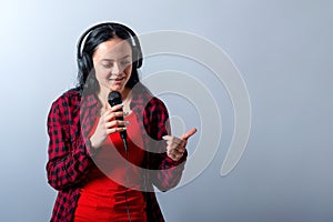 Cheerful young woman in casual clothes with headphones sing song in microphone, mock up, copy space