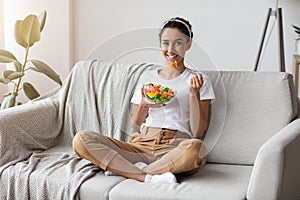 Cheerful young woman eating vegetable salad at home