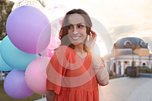 Cheerful young woman with color balloons on sunny day