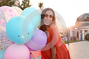 Cheerful young woman with color balloons on sunny day