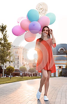 Cheerful young woman with color balloons on sunny day