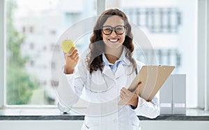 Cheerful young woman doctor holding apple and clipboard