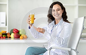 Cheerful young woman doctor showing glass with fresh juice