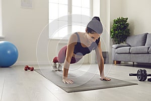 Cheerful young woman doing full plank on sports mat during fitness workout at home