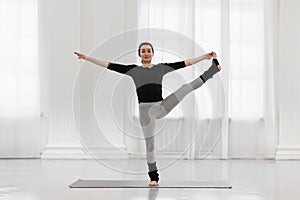 Cheerful young woman doing utthita hasta padagusthasana in the gym while yoga classes. Concept of flexibility, leg and