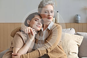 Cheerful young woman is embracing her middle aged mother with closed eyes hugging, touching cheeks