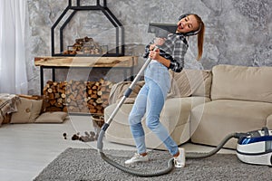 Cheerful young woman enjoying solo singing with vacuum cleaner while cleaning house