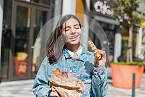 cheerful young woman enjoying tasty waffles in front of a cafe in the street. take away food in the city