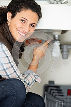 cheerful young woman fixing leaking sink pipe in kitchen