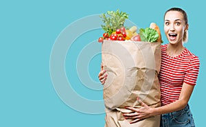 Cheerful young woman holding a grocery bag filled with vegetable