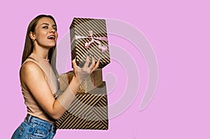 Cheerful young woman holding heap of presents, looking at camera, isolated on pink background