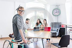 Cheerful young woman holding her commuter bike in a shared office