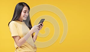 Cheerful young woman holding smartphone and her hand with shocked amazed for success or get good news over isolated yellow