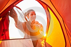 Cheerful young woman in hoodie unzipping camp tent