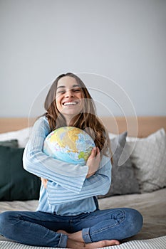 Cheerful young woman hugging globe sitting on the couch at home