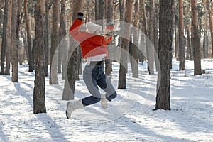 Cheerful young woman jumps high in snowy forest. Walk through the winter wood on sunny day