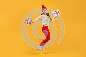 Cheerful young woman jumps with Xmas gift boxes, yellow backdrop