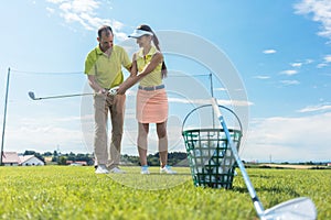 Cheerful young woman learning the correct grip and move for using the golf club