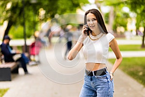 Cheerful young woman looking down on street while talking over smartphone. Smiling girl walking on street and talking on phone
