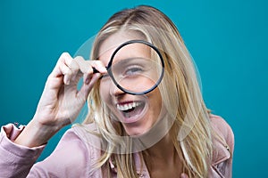 Cheerful young woman looking through magnifying glass isolated over blue background