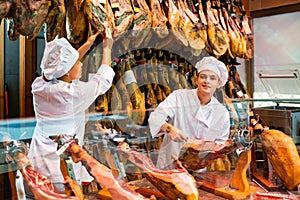 Cheerful young woman and man selling ham in jamoneria