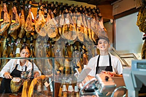 Cheerful young woman and man selling ham in jamoneria