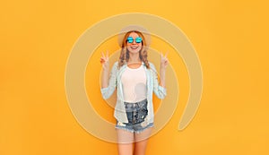 Cheerful young woman posing wearing summer straw hat and shorts on orange background